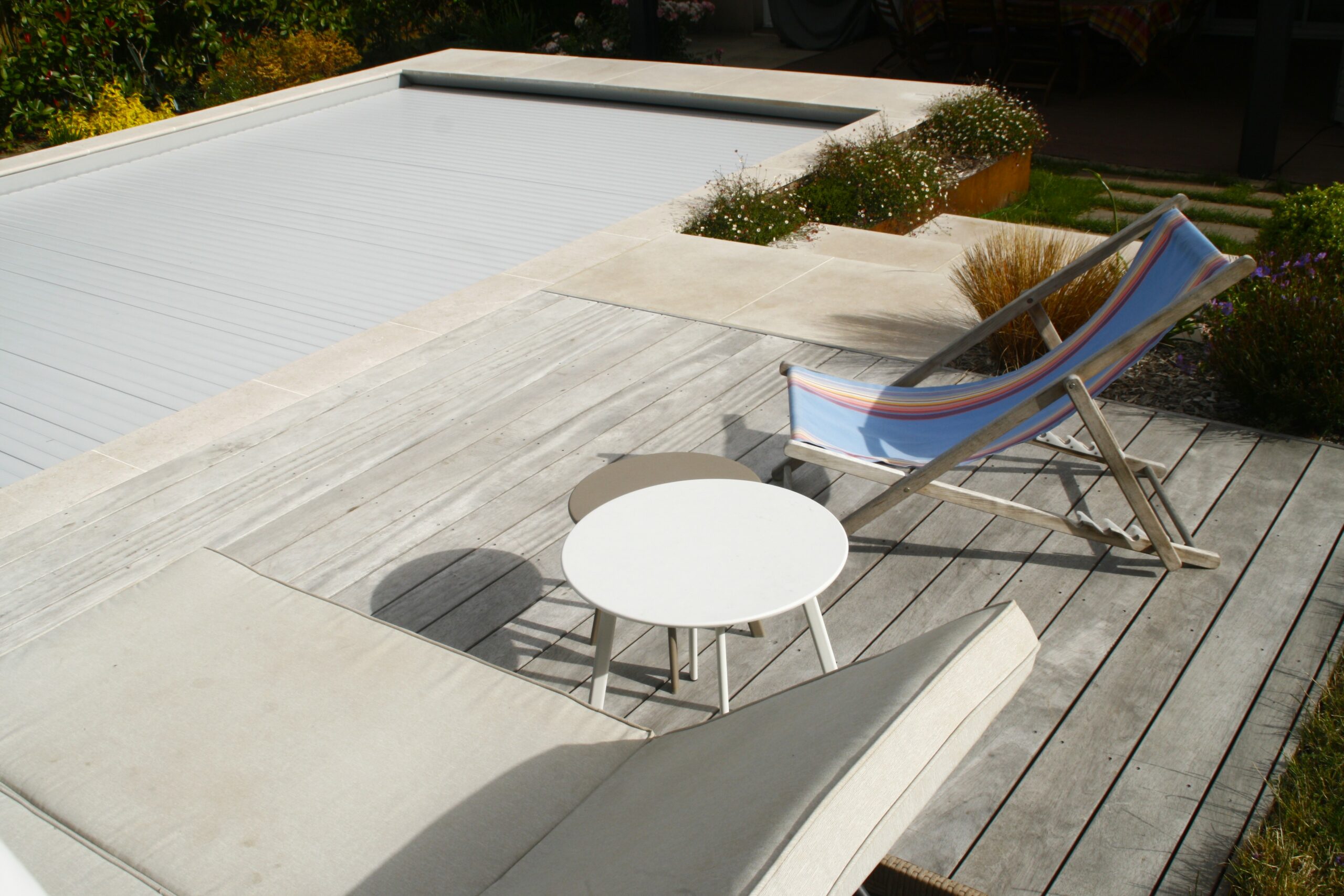 Aménagement autour de la piscine avec une terrasse en padouk, des emmarchements en céramique et des jardinières corten avec des plantations - Haie-Fouassière